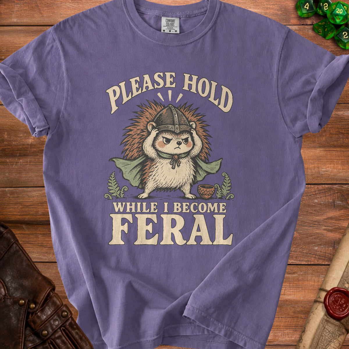 Purple t-shirt with a hedgehog wearing a helmet and cape, and text "PLEASE HOLD WHILE I BECOME FERAL".
