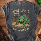 T-shirt with green goblin character, stacks of books, and text "LORE UPDATE I'M LOSING IT".