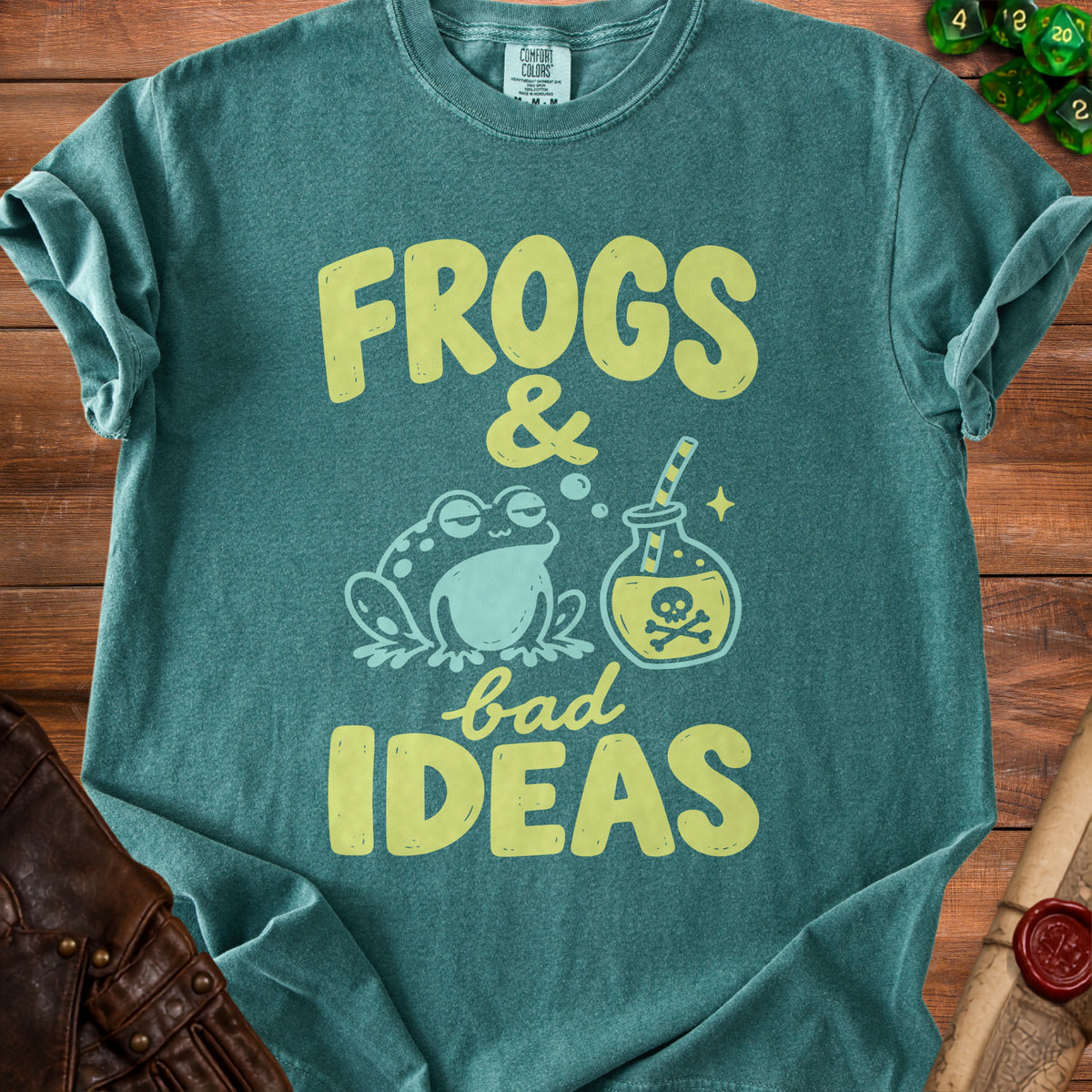 Dark green t-shirt featuring the text Frogs and bad ideas alongside a frog and a potion bottle.