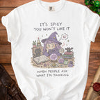 White t-shirt with illustration of a witch and witchy items, text reads "It's Spicy You Won't Like It When People Ask What I'm Thinking."
