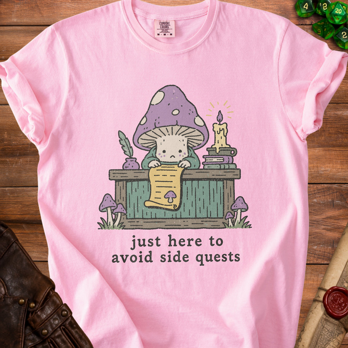 Pink t-shirt with a cartoon mushroom reading a scroll, text says "just here to avoid side quests".