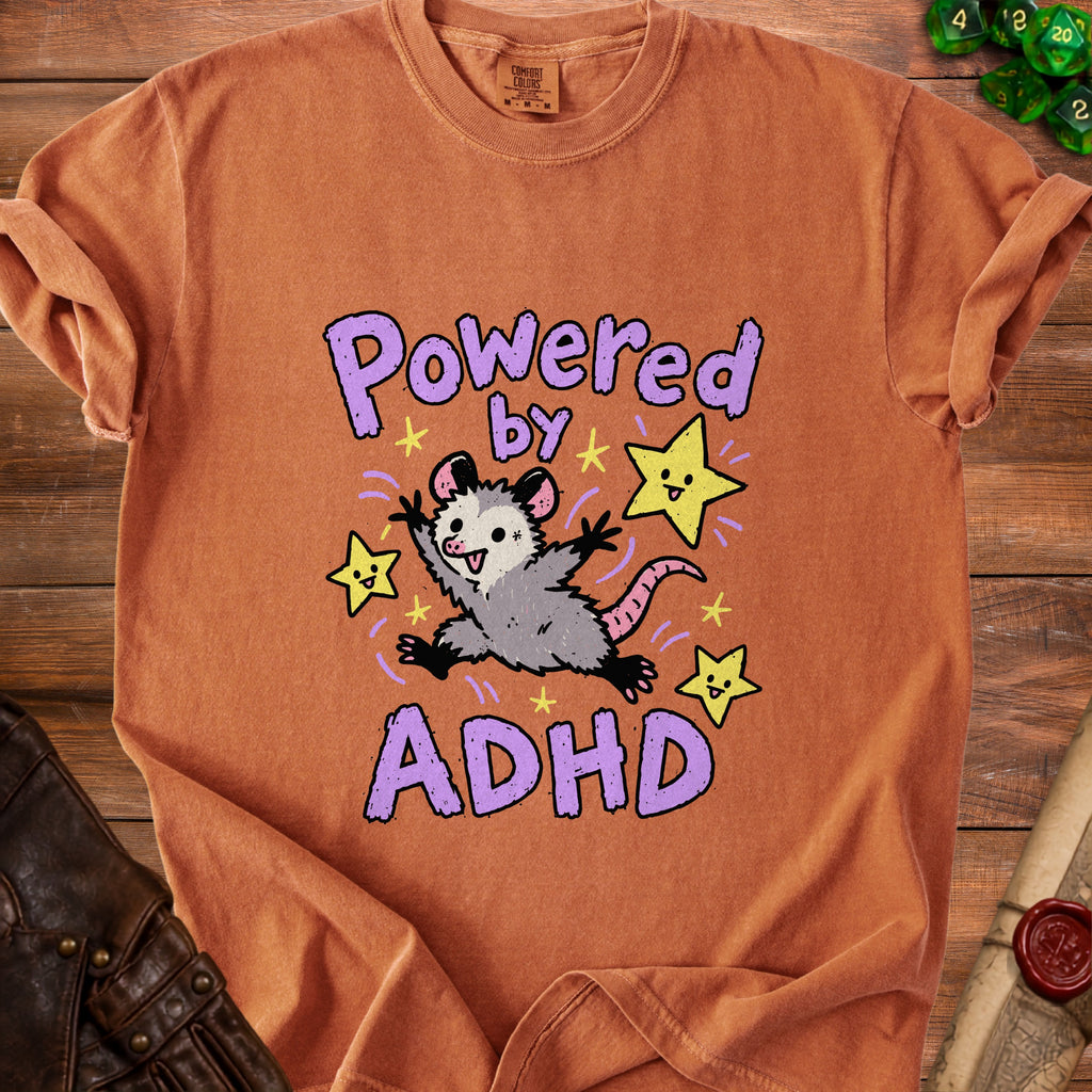 Orange t-shirt with a cartoon possum and stars saying "Powered by ADHD."