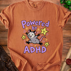 Orange t-shirt with a cartoon possum and stars saying "Powered by ADHD."