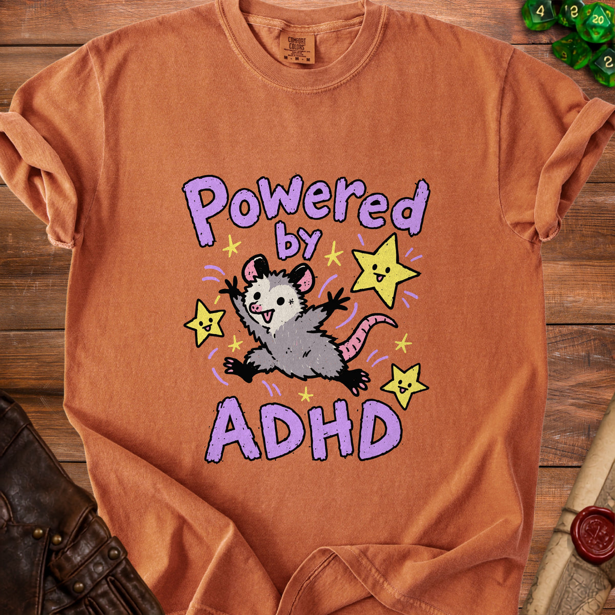 Orange t-shirt with a cartoon possum and stars saying "Powered by ADHD."