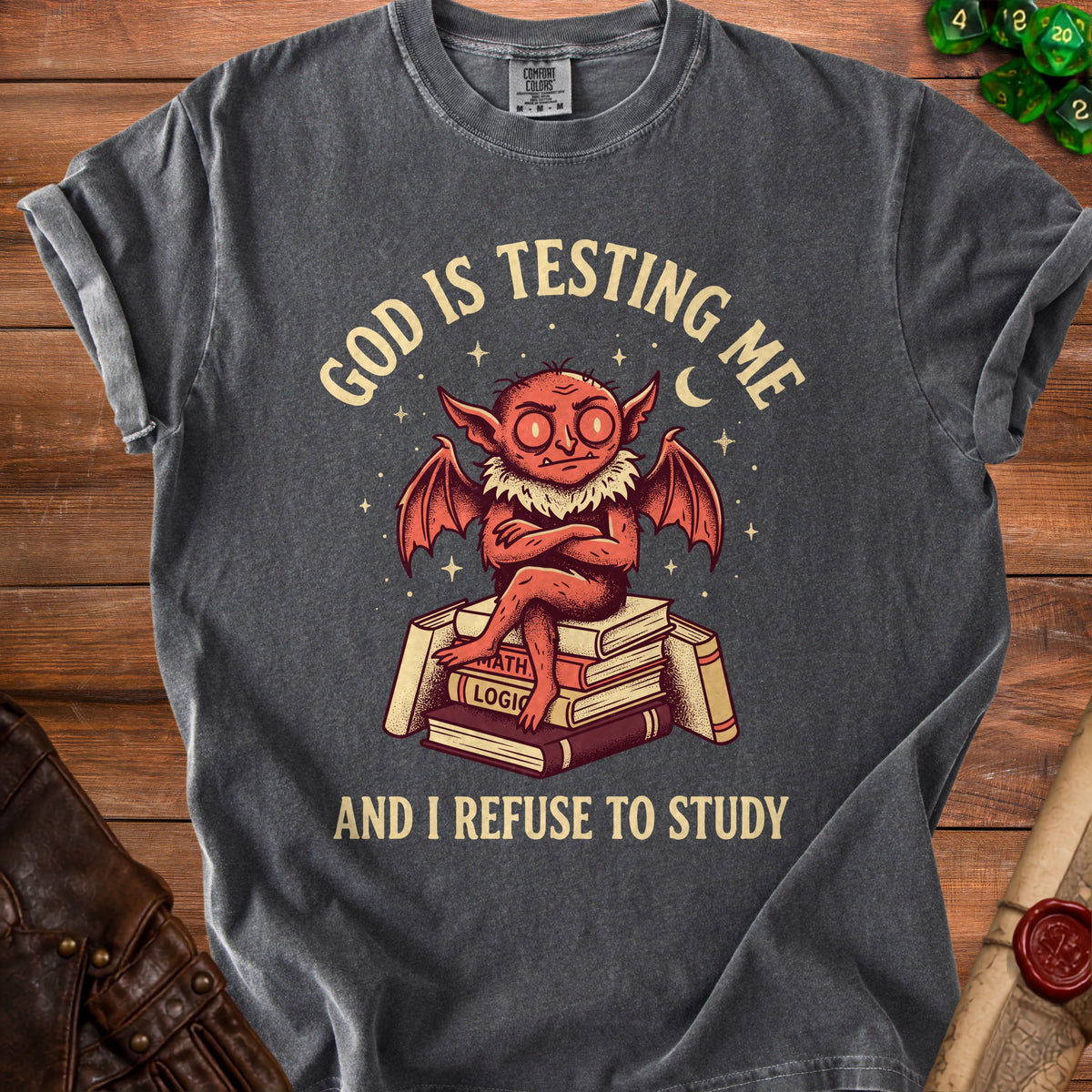 Dark gray t-shirt with devil sitting on books, text reads "GOD IS TESTING ME AND I REFUSE TO STUDY".