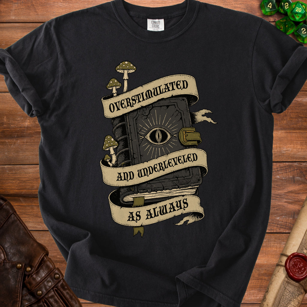 Black t-shirt with a vintage graphic of a spellbook and mushrooms, text reads "Overstimulated and Underleveled as Always".