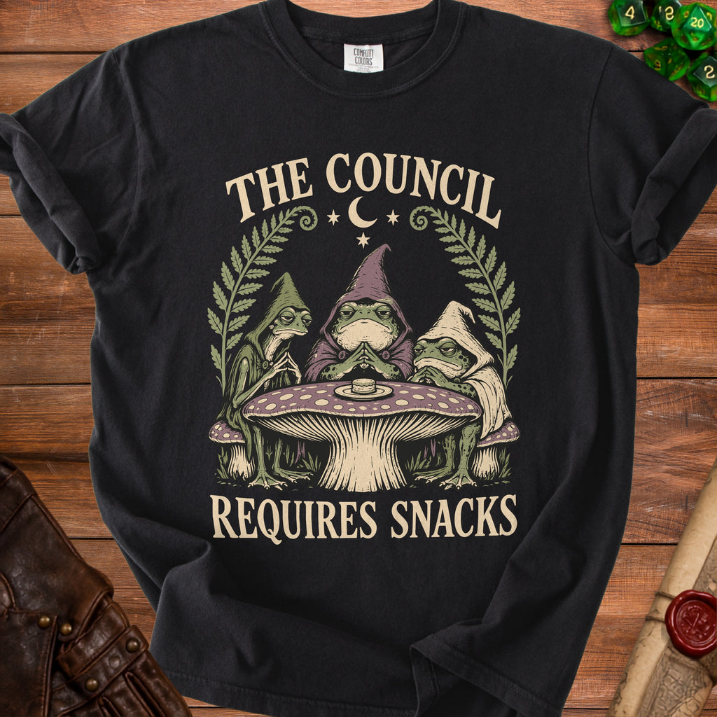 T-shirt graphic of three robed frogs at a mushroom table, text reads "The Council Requires Snacks".