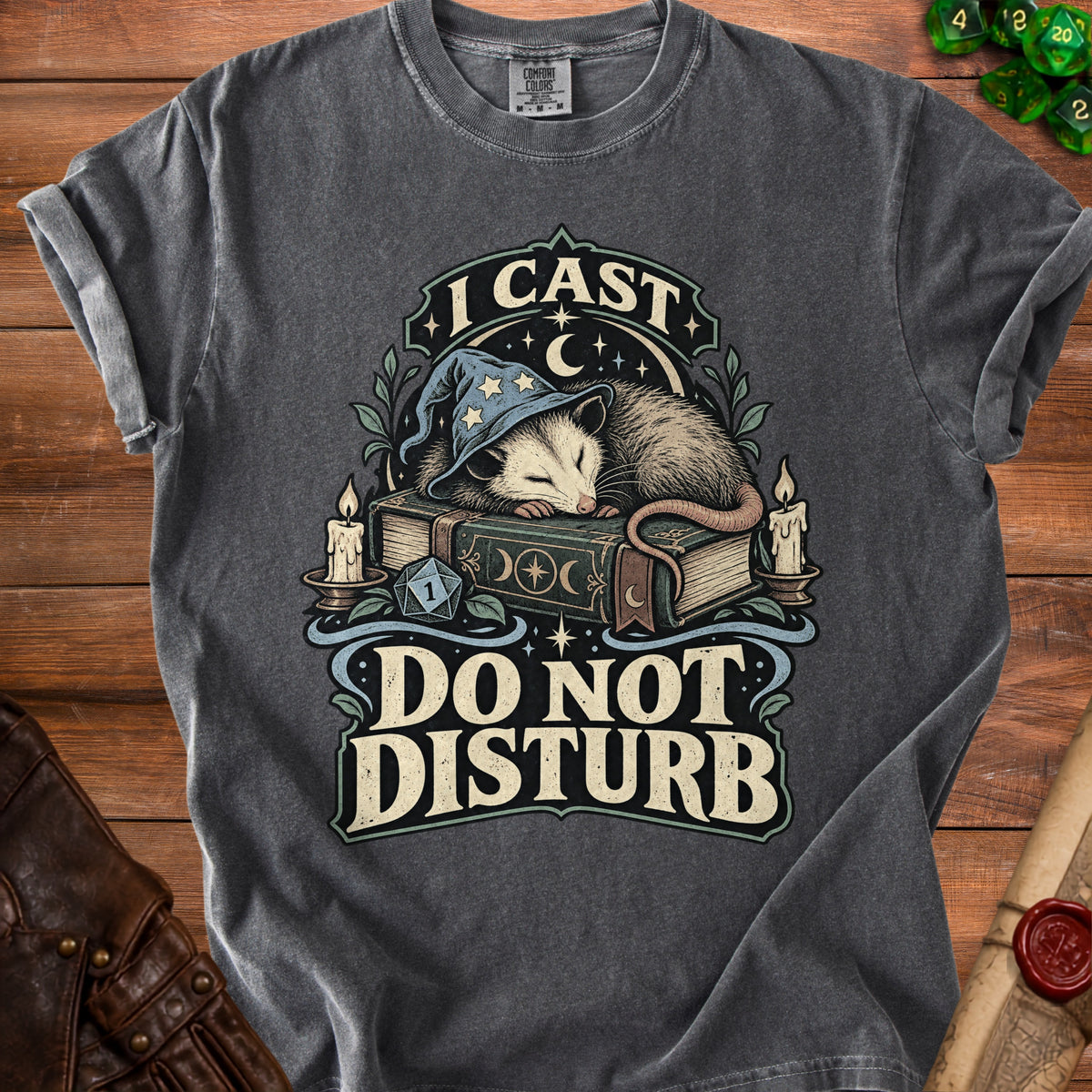 A dark gray t-shirt featuring a graphic of an opossum in a wizard hat sleeping on a book with the text "I CAST DO NOT DISTURB."