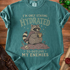 Teal t-shirt with a raccoon drinking from a goblet, stating "I'm only staying hydrated to outlive my enemies".