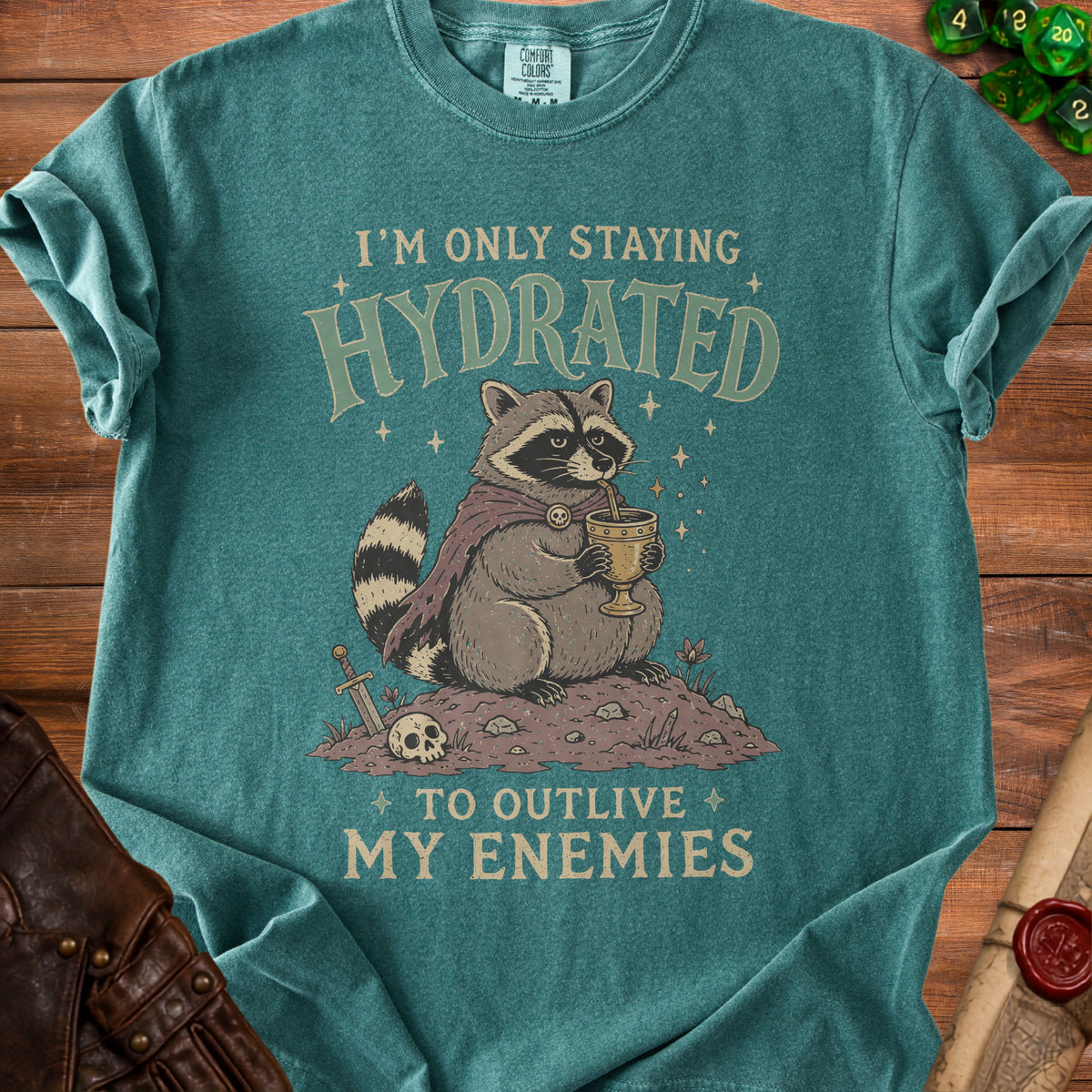Teal t-shirt with a raccoon drinking from a goblet, stating "I'm only staying hydrated to outlive my enemies".
