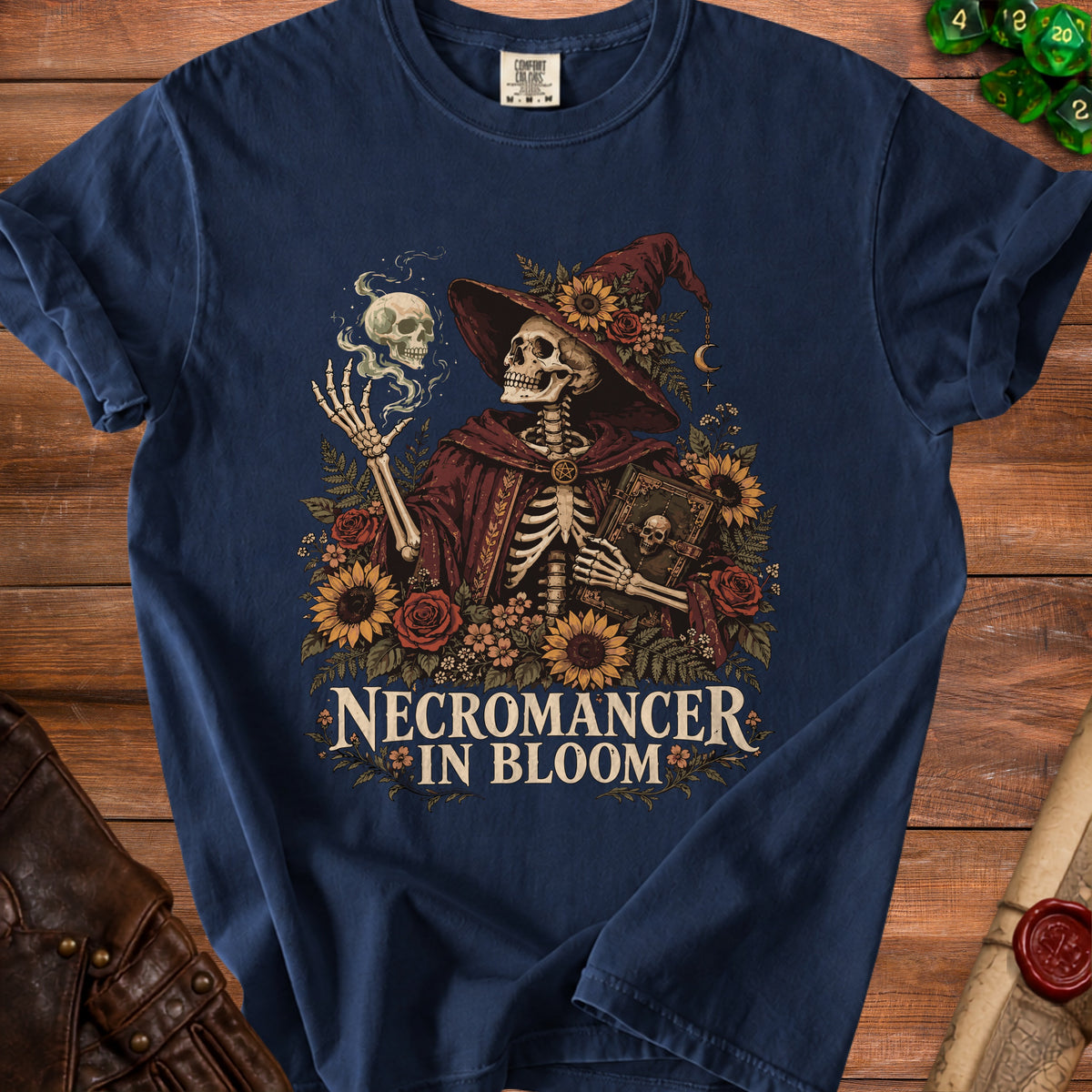 Navy t-shirt with a skeleton necromancer, skulls, and flowers, text "NECROMANCER IN BLOOM".