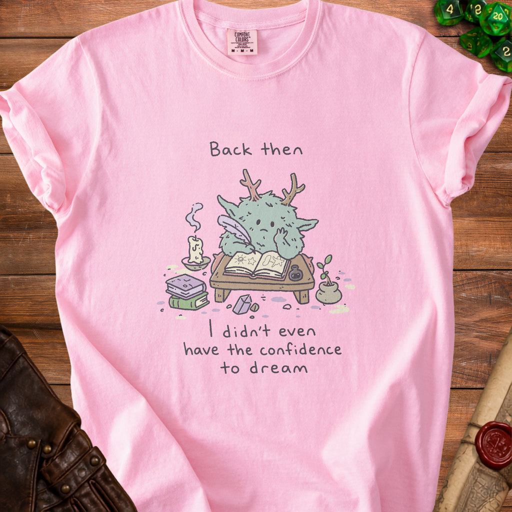 Pink t-shirt with a green creature writing: "Back then I didn't even have the confidence to dream."