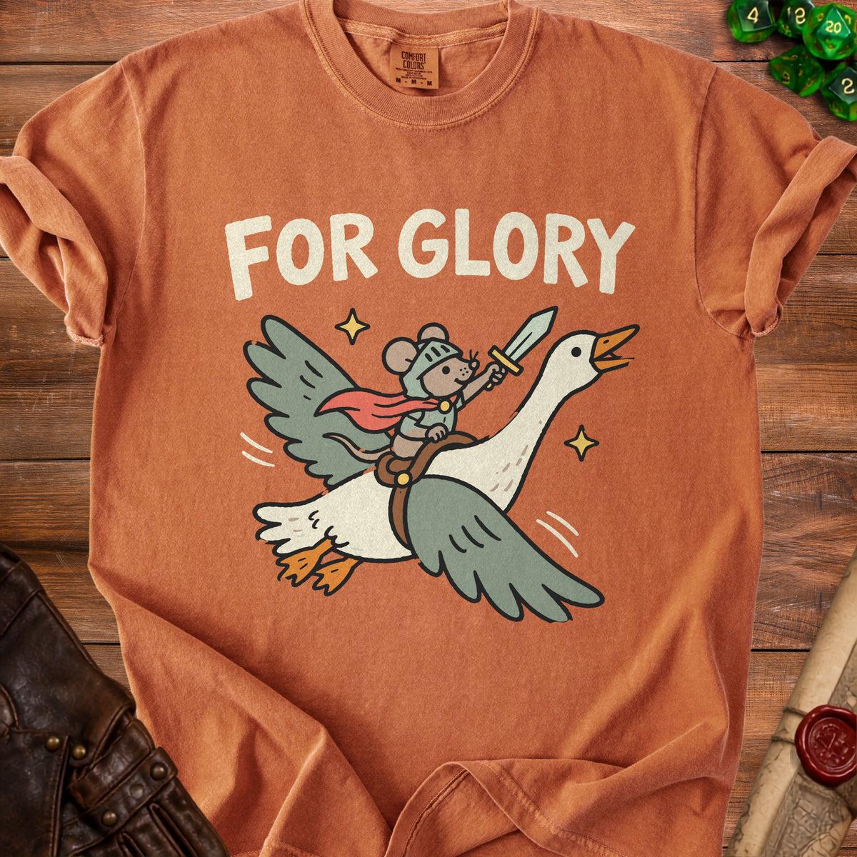 A rust-colored t-shirt with a graphic of a mouse knight riding a flying goose, with text that reads FOR GLORY.