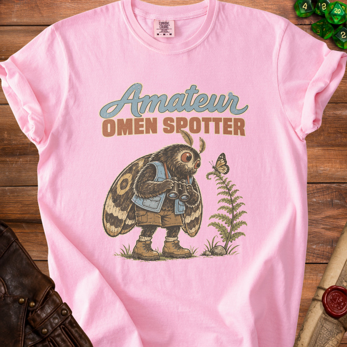 Pink t-shirt with "Amateur Omen Spotter" text and a moth character holding binoculars.