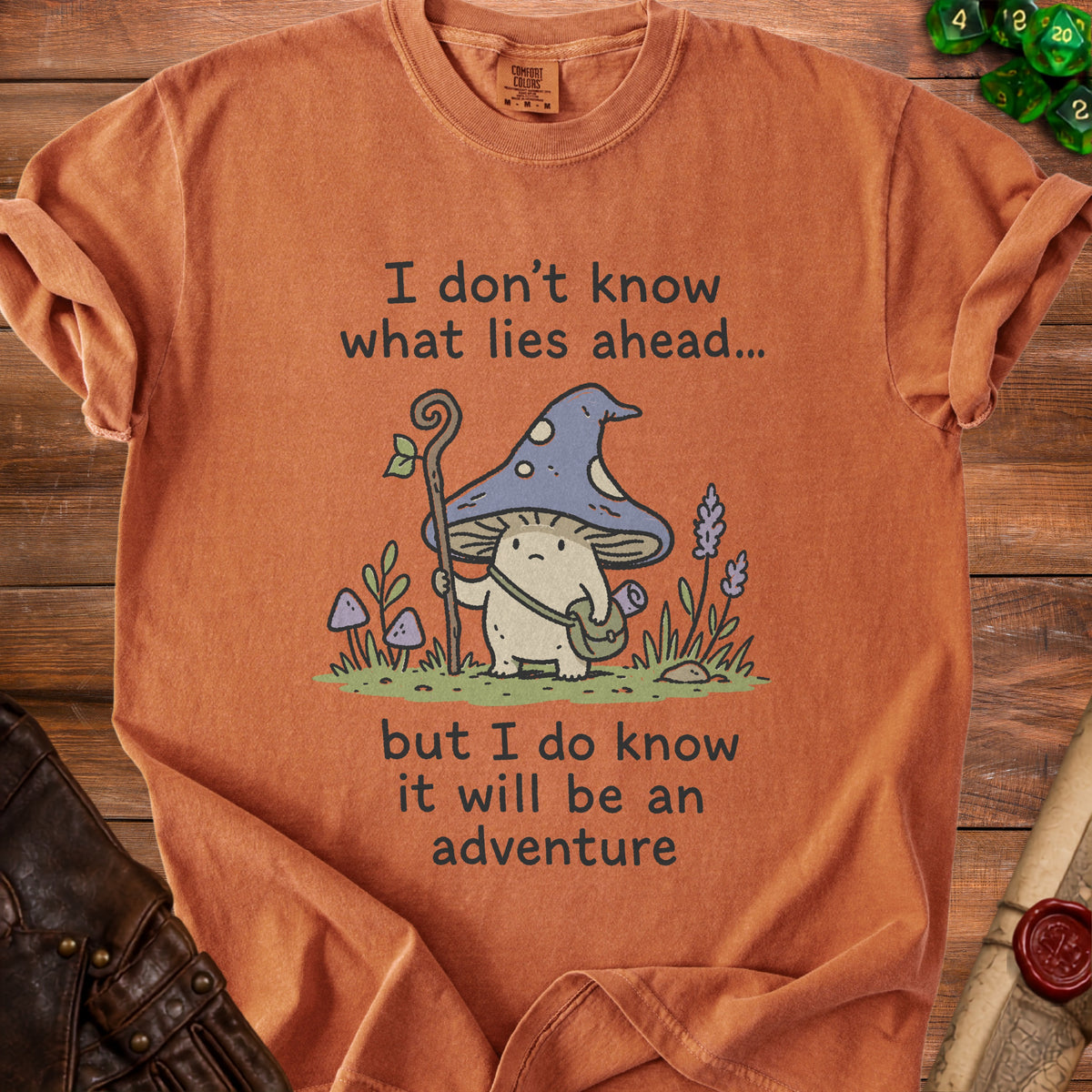 Orange t-shirt with a mushroom character and text reading "I don't know what lies ahead... but I do know it will be an adventure".
