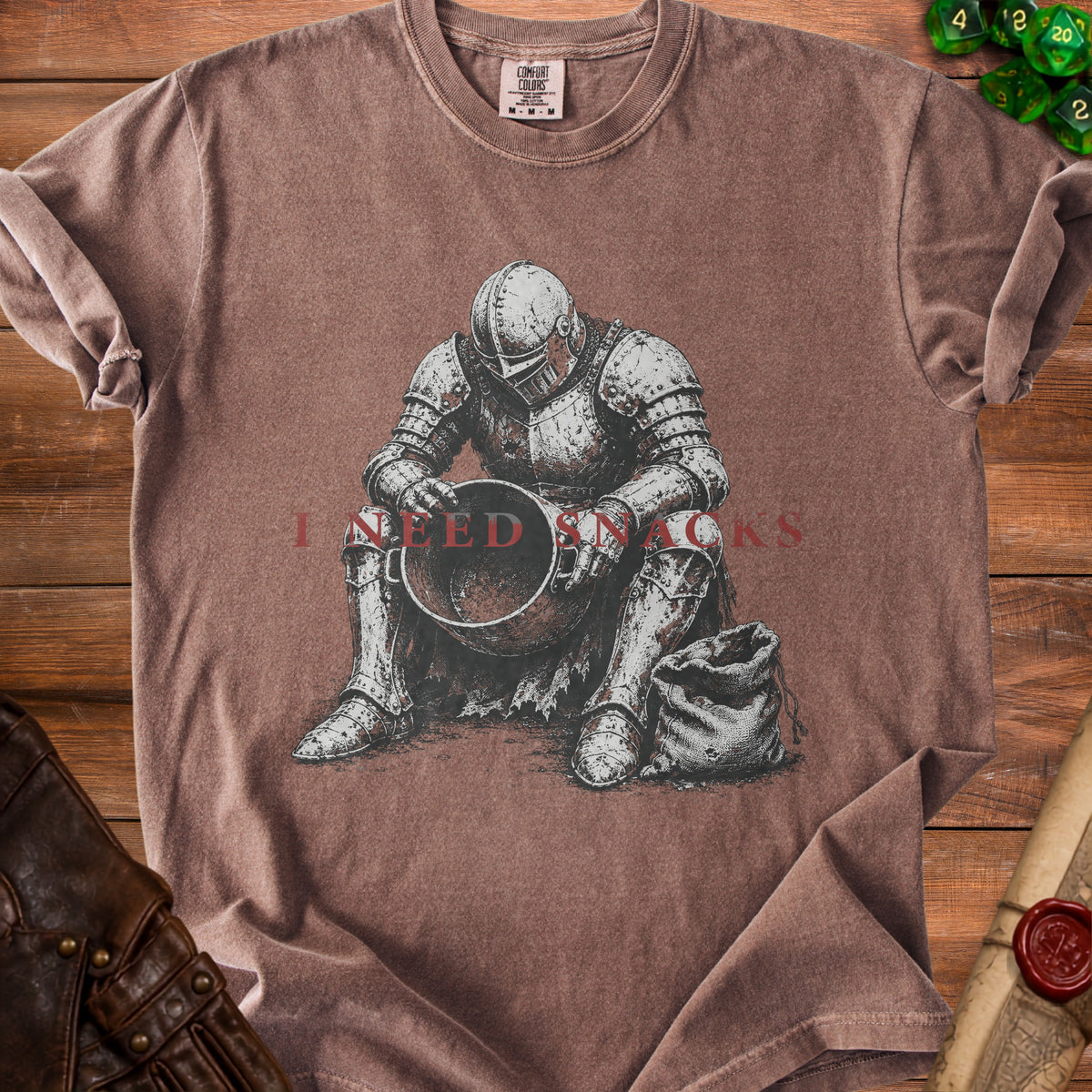 T-shirt with illustration of knight sitting with bowl and sack, text "I NEED SNACKS".