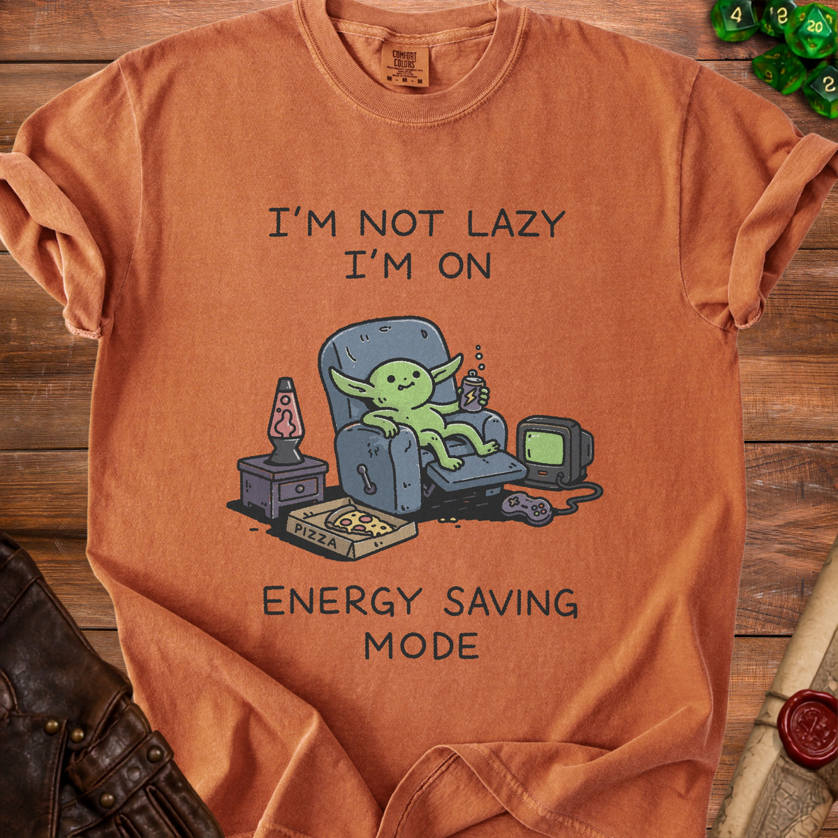 Orange t-shirt with cartoon character sitting in chair, holding drink, with pizza and video game controller.