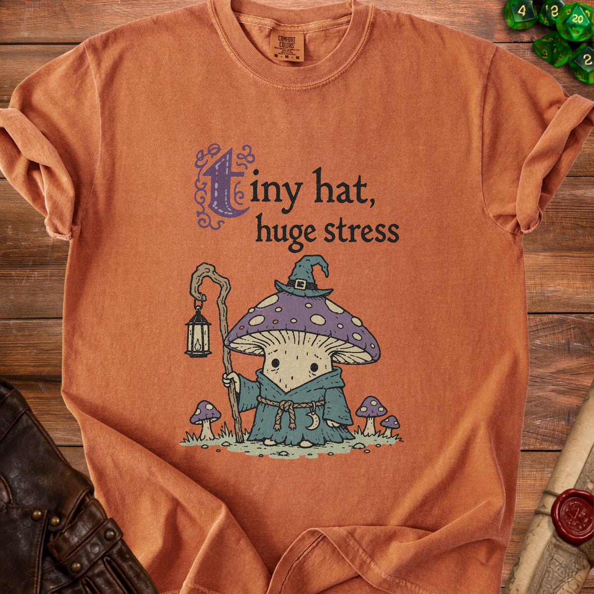 Orange t-shirt with "tiny hat, huge stress" text and mushroom wizard graphic.