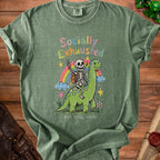 Skeleton riding a dinosaur under a rainbow with "Socially Exhausted But Still Here" text.