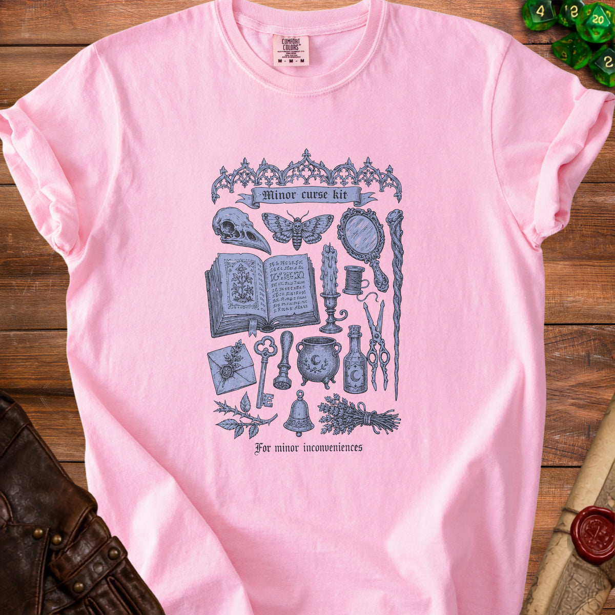 Pink t-shirt with a "Minor curse kit" graphic featuring a skull, moth, and magical items.
