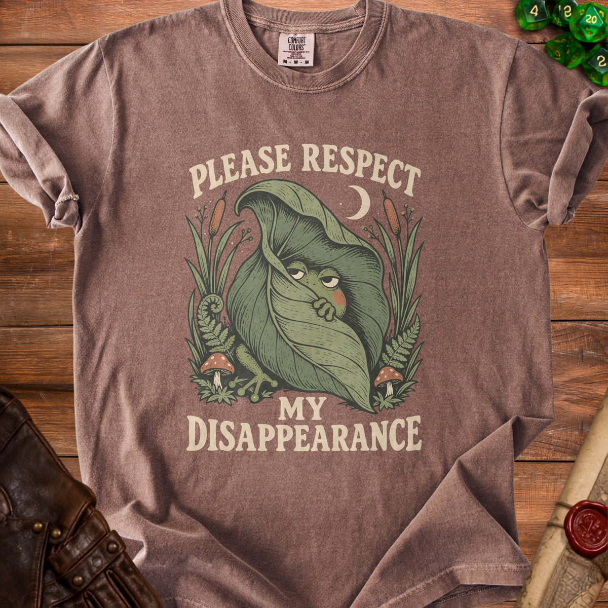 Brown t-shirt with a cartoon frog peeking from a leaf, text says "Please Respect My Disappearance".