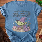 Blue t-shirt with graphic of a grumpy goblin and text: "Today's priorities are peace, snacks, and fewer opinions."