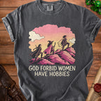 Charcoal gray t-shirt featuring an illustration of three fantasy women climbing a hill with the text GOD FORBID WOMEN HAVE HOBBIES.
