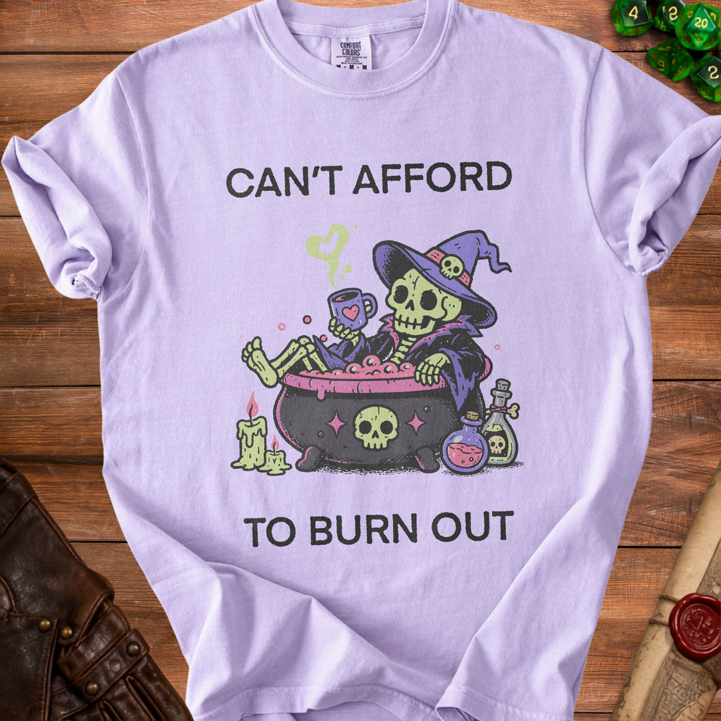 Lilac t-shirt with a skeleton witch in a cauldron and text reading "Can't Afford To Burn Out".