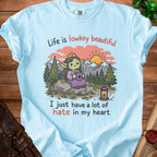 Light blue t-shirt with a graphic of a crowned goblin drinking coffee with the text "Life is lowkey beautiful I just have a lot of hate in my heart".