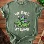 Green t-shirt with goblin riding alligator graphic and text "WE RIDE AT DAWN".