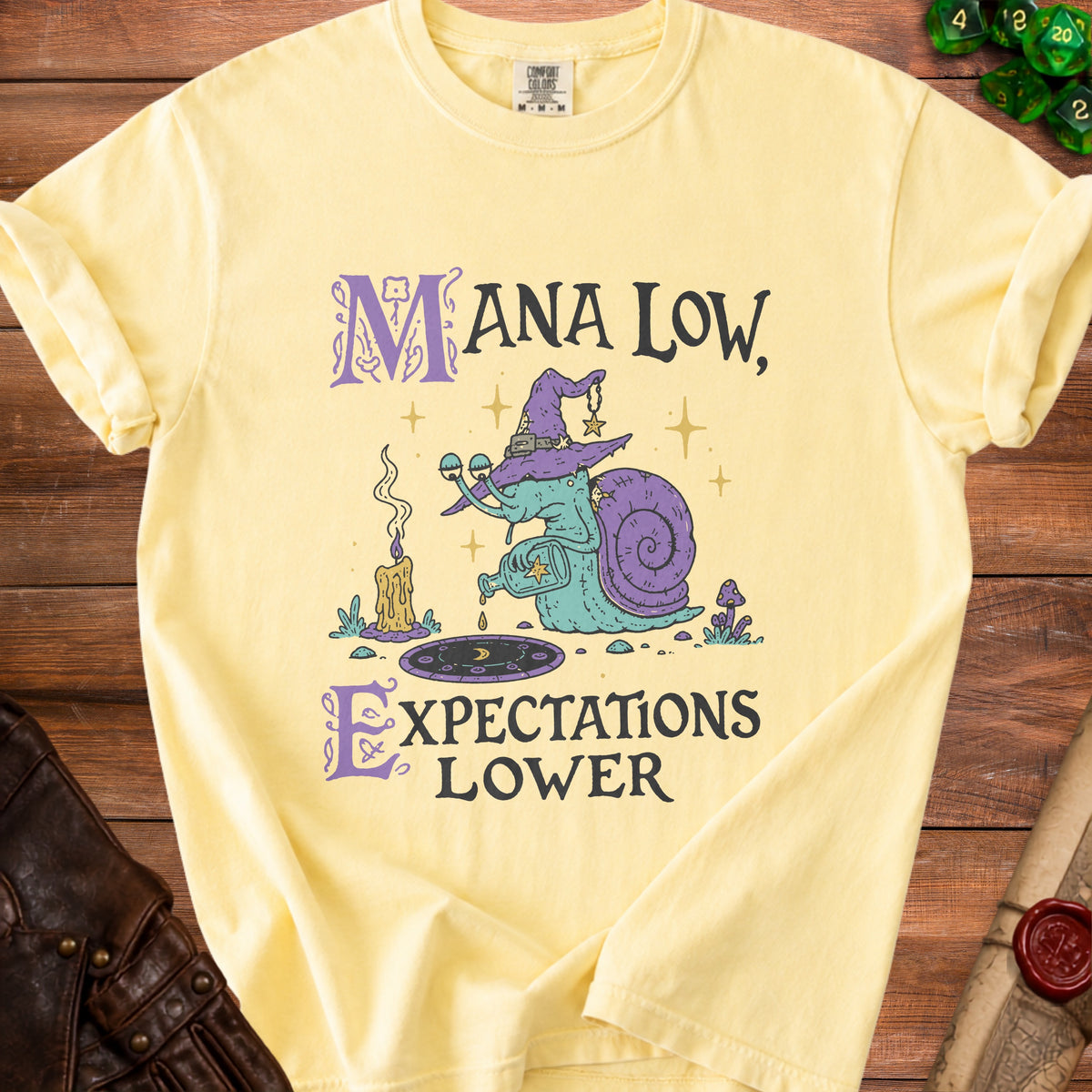 Yellow t-shirt with a wizard snail pouring potion and text "Mana Low, Expectations Lower".