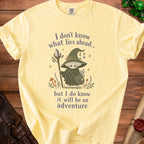 Yellow t-shirt with a mushroom character holding a staff and the text "I don't know what lies ahead... but I do know it will be an adventure".