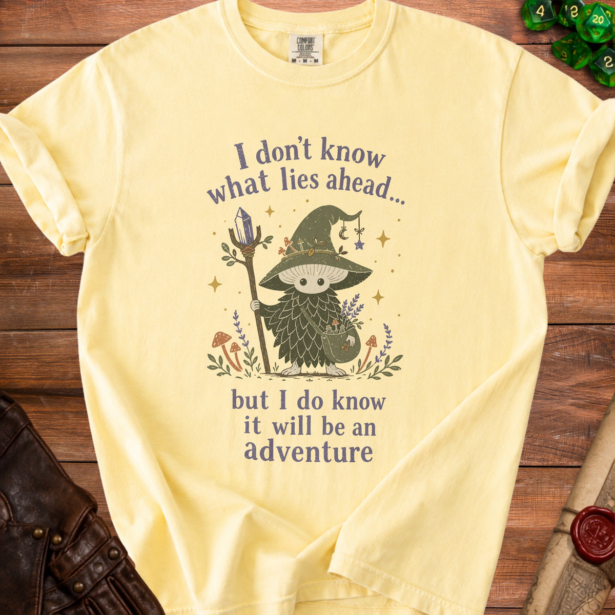 Yellow t-shirt with a mushroom character holding a staff and the text "I don't know what lies ahead... but I do know it will be an adventure".
