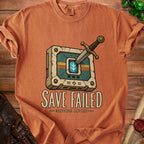 Orange t-shirt with a sword stuck in a cracked, retro-futuristic console that reads "SAVE FAILED - CONTINUE ANYWAY".