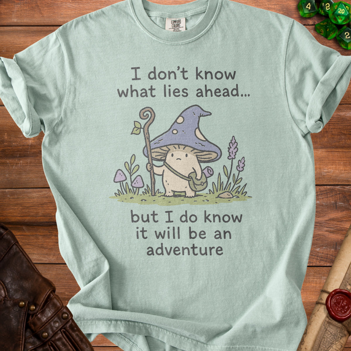 Light mint t-shirt with a mushroom character graphic and text reading "I don't know what lies ahead... but I do know it will be an adventure".