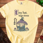 Yellow t-shirt with "tiny hat, huge stress" text and mushroom wizard graphic.