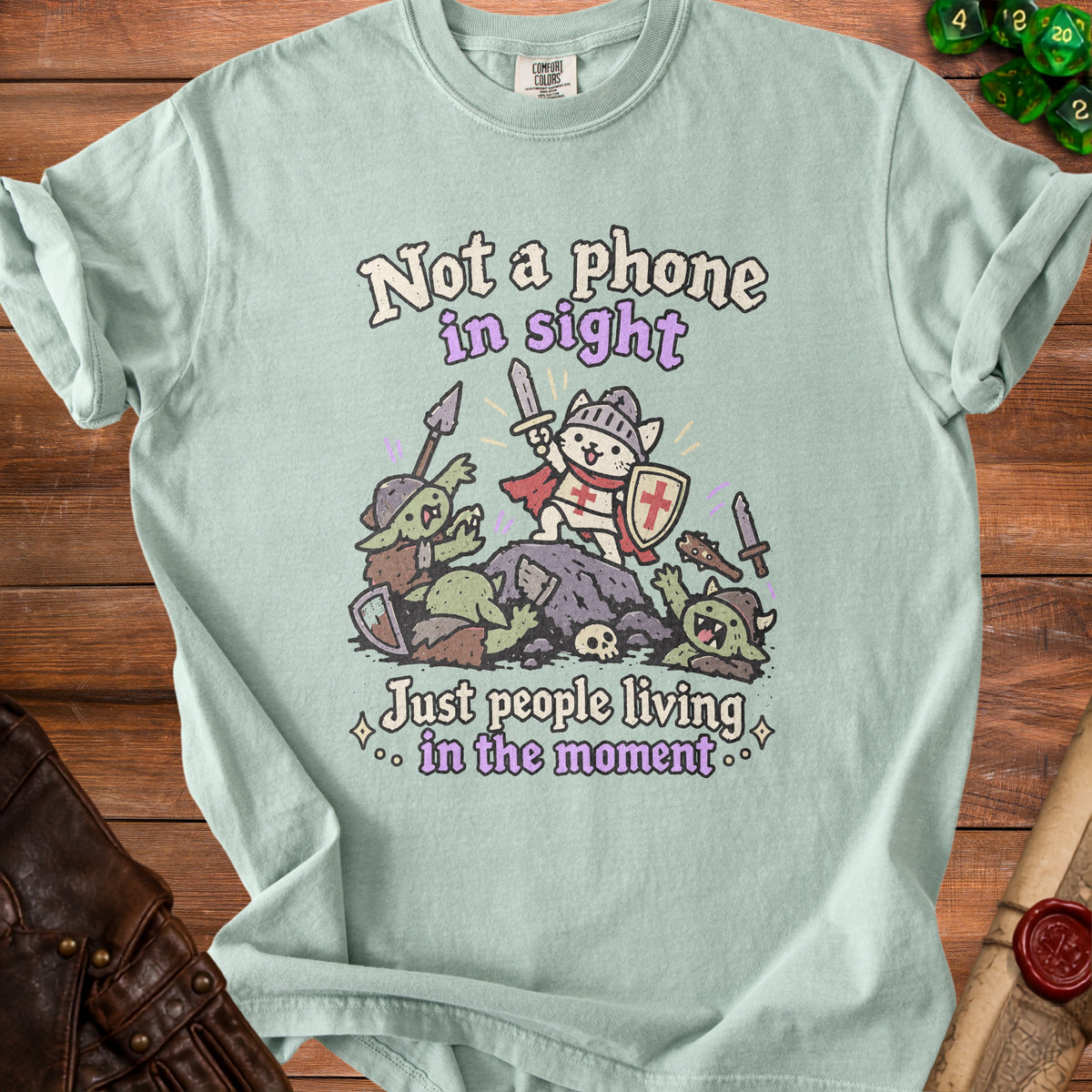 Light blue t-shirt with knights and goblins graphic and text "Not a phone in sight, Just people living in the moment".