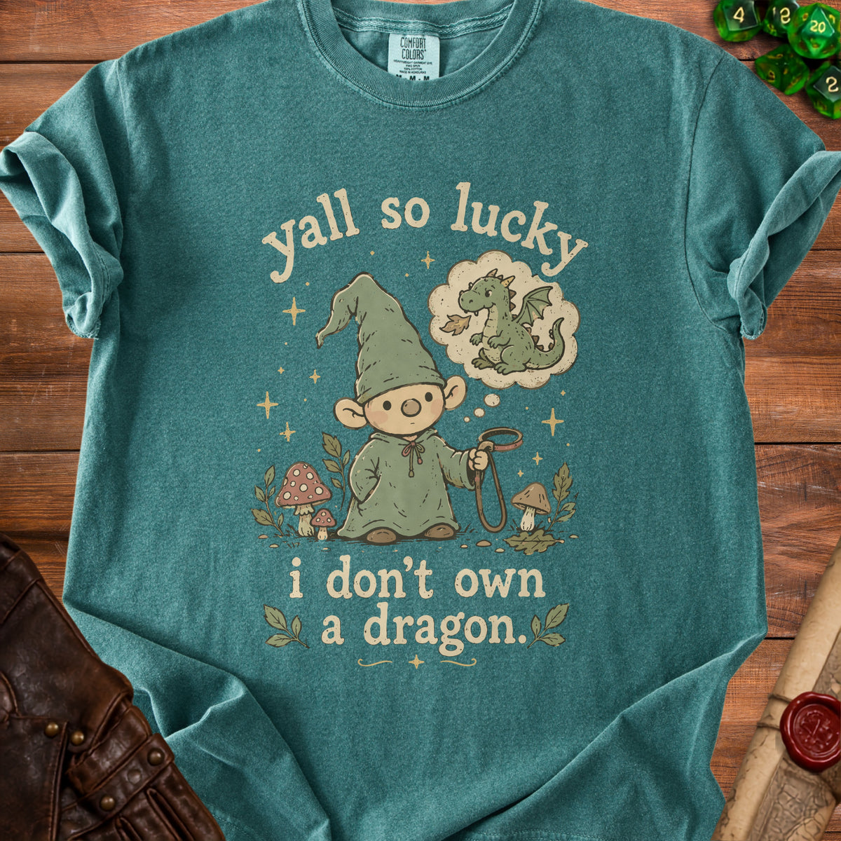 Teal t-shirt with gnome holding leash, thinking of dragon. Text reads "yall so lucky i don't own a dragon."