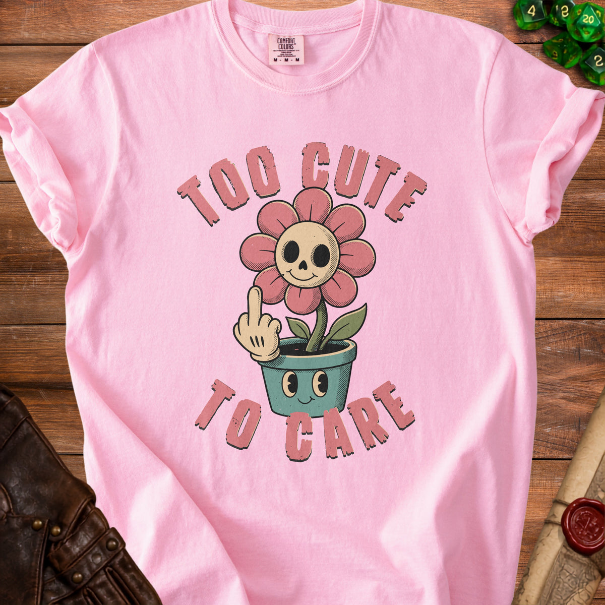 Pink t-shirt with graphic text "TOO CUTE TO CARE" and a skull-faced flower.