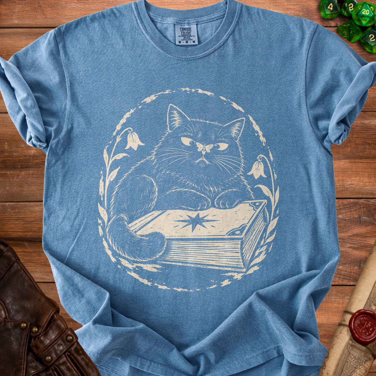 Blue t-shirt with a cream-colored graphic of a cat sitting on a book.