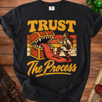 Black t-shirt with "TRUST The Process" text and illustration of a man giving a thumbs up to a treasure chest monster.
