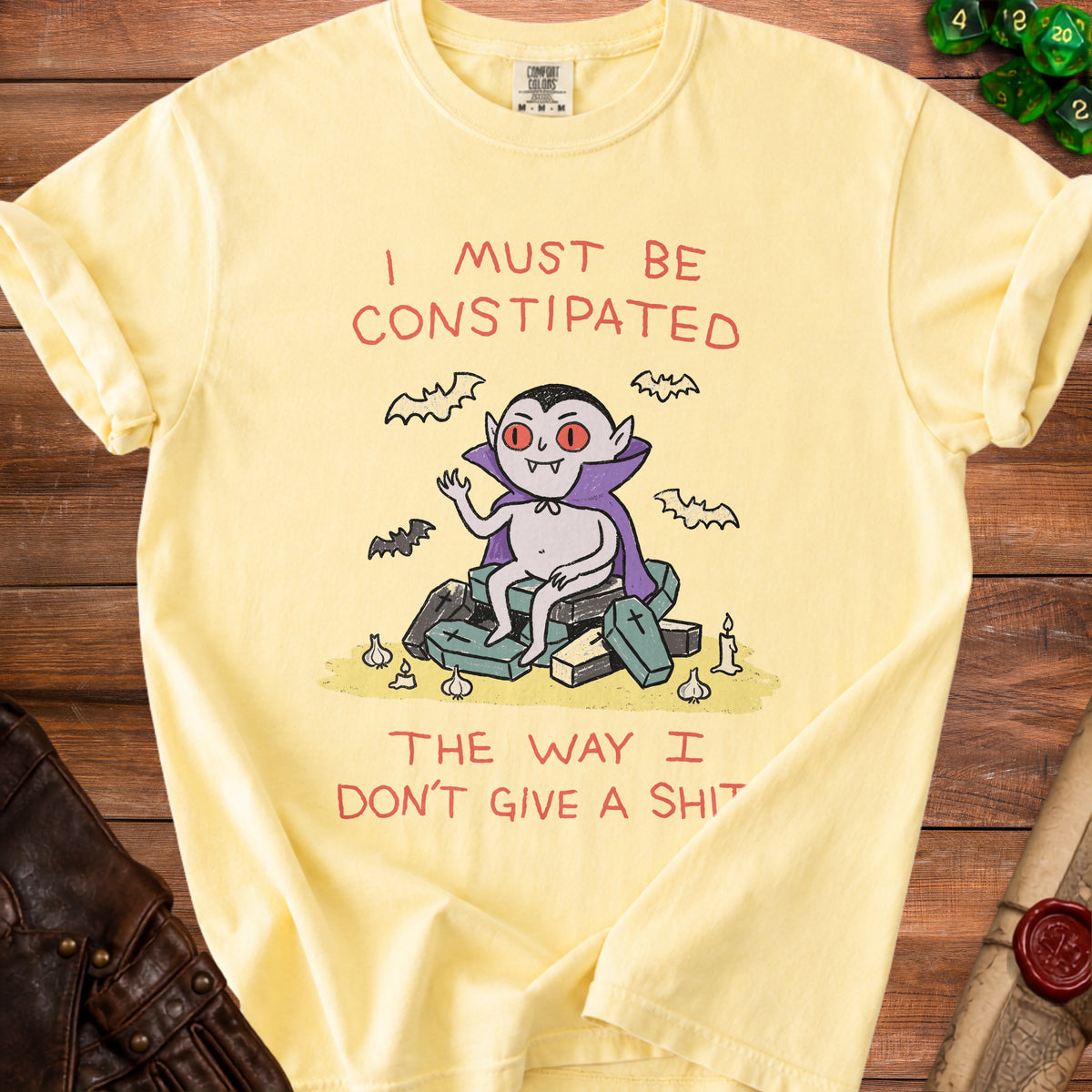 Yellow t-shirt with a cartoon vampire sitting on coffins and text "I must be constipated the way I don't give a shit."