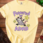 Yellow t-shirt with opossum graphic that says "Powered by ADHD" and stars.