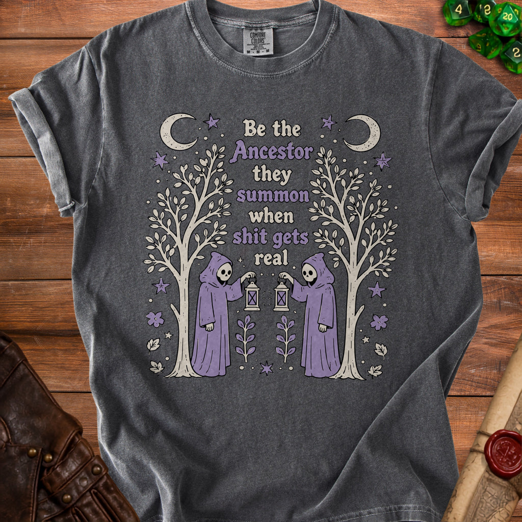 Dark grey t-shirt with a graphic of two grim reapers holding lanterns and the text "Be the Ancestor they summon when shit gets real".