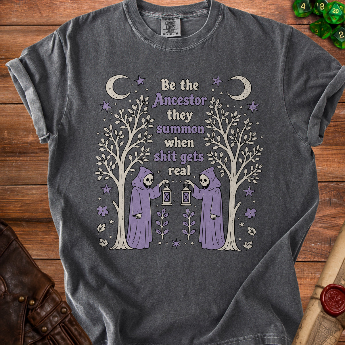 Dark grey t-shirt with a graphic of two grim reapers holding lanterns and the text "Be the Ancestor they summon when shit gets real".