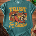 Graphic t-shirt with text "TRUST The Process", a treasure chest, and a stylized adventurer.