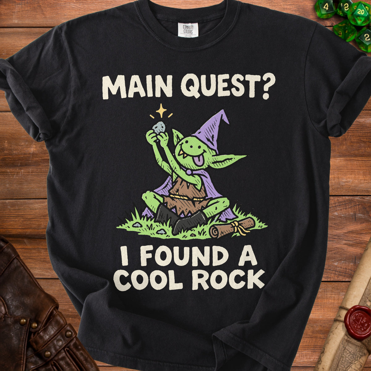 Black t-shirt with a cartoon goblin holding a rock, text reads "MAIN QUEST? I FOUND A COOL ROCK".