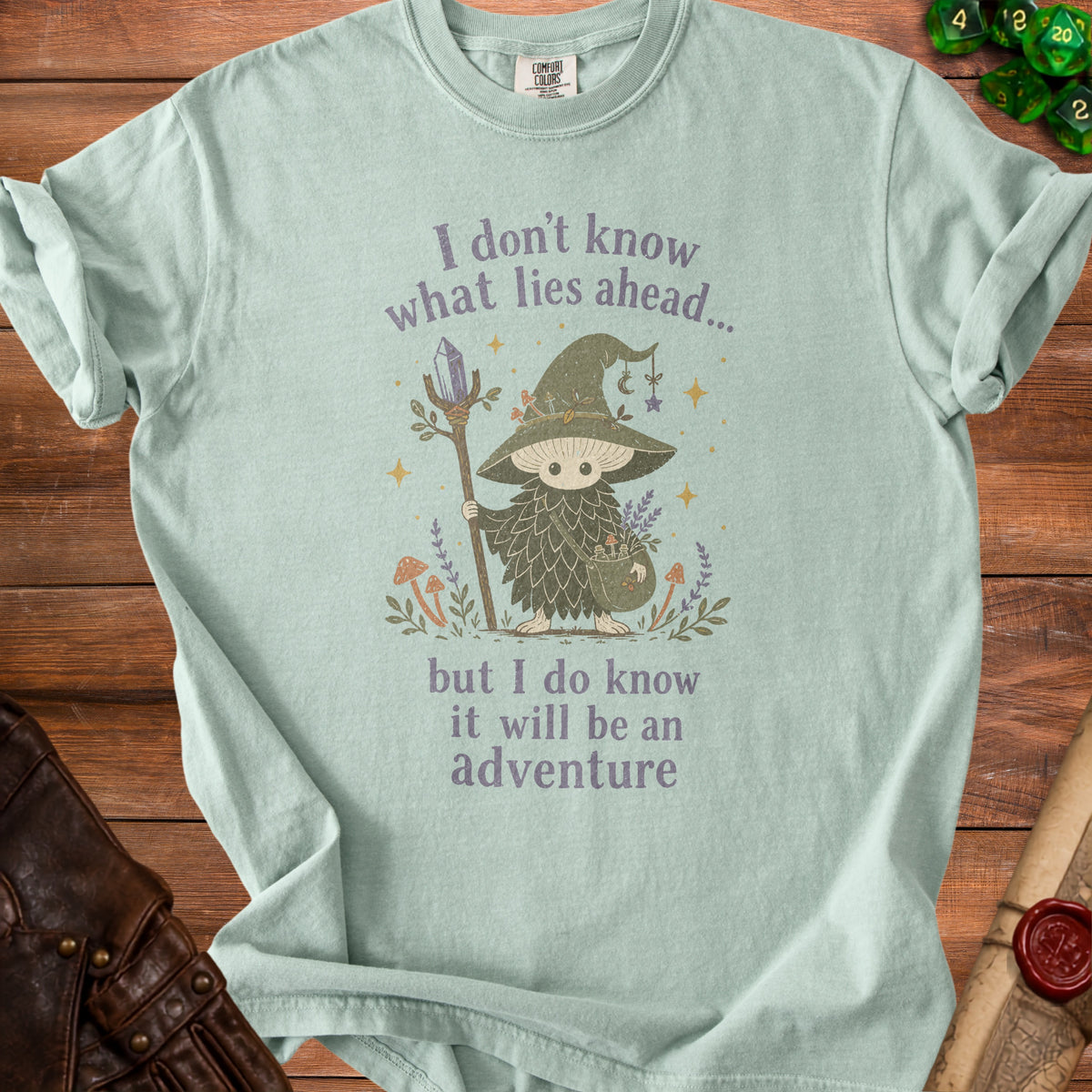 Light green t-shirt with "I don't know what lies ahead... but I do know it will be an adventure" text and mushroom wizard graphic.