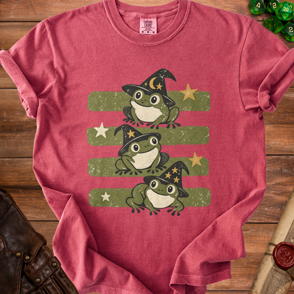 Three frogs in witch hats with stars and moons on a striped background.