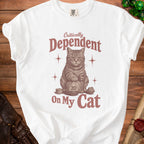 White t-shirt with a graphic of a cat and dice, reading "Critically Dependent On My Cat."
